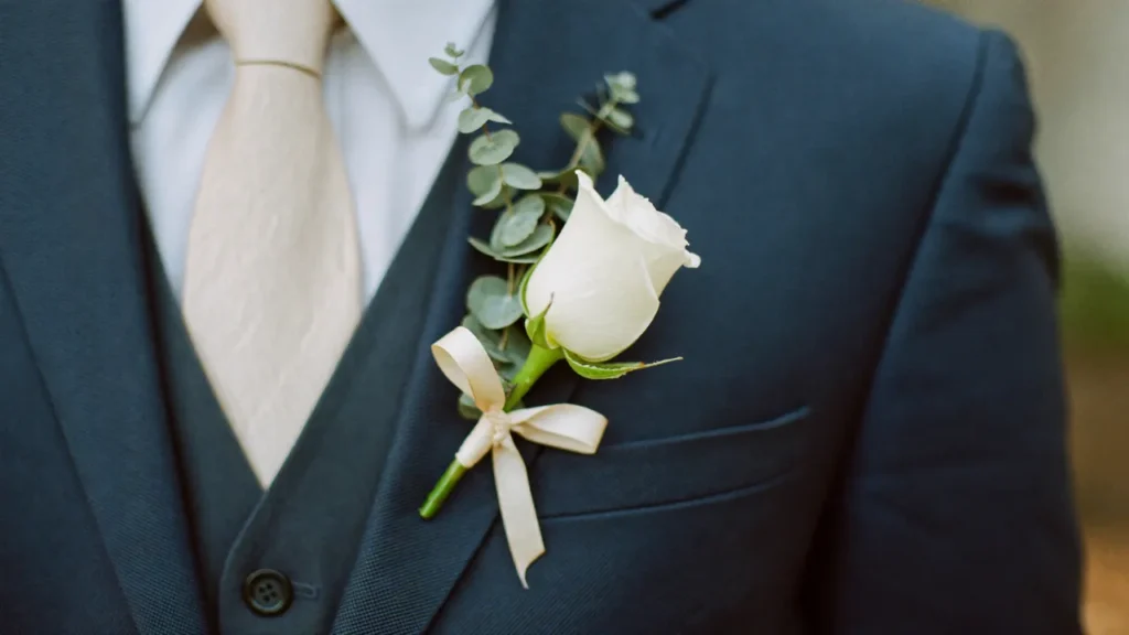 Boutonnière de mariage rose blanche et eucalyptus sur revers de costume bleu nuit