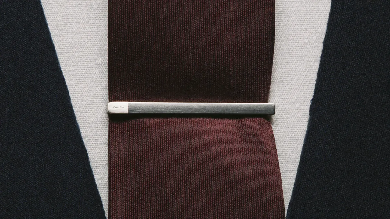 Pince à cravate argent sur cravate bordeaux soie et chemise blanche sous costume marine